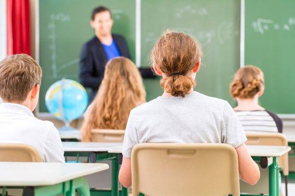 Teacher or educator or docent standing while lesson  in front of a blackboard and educate or teach students or pupils or mates in a school or class